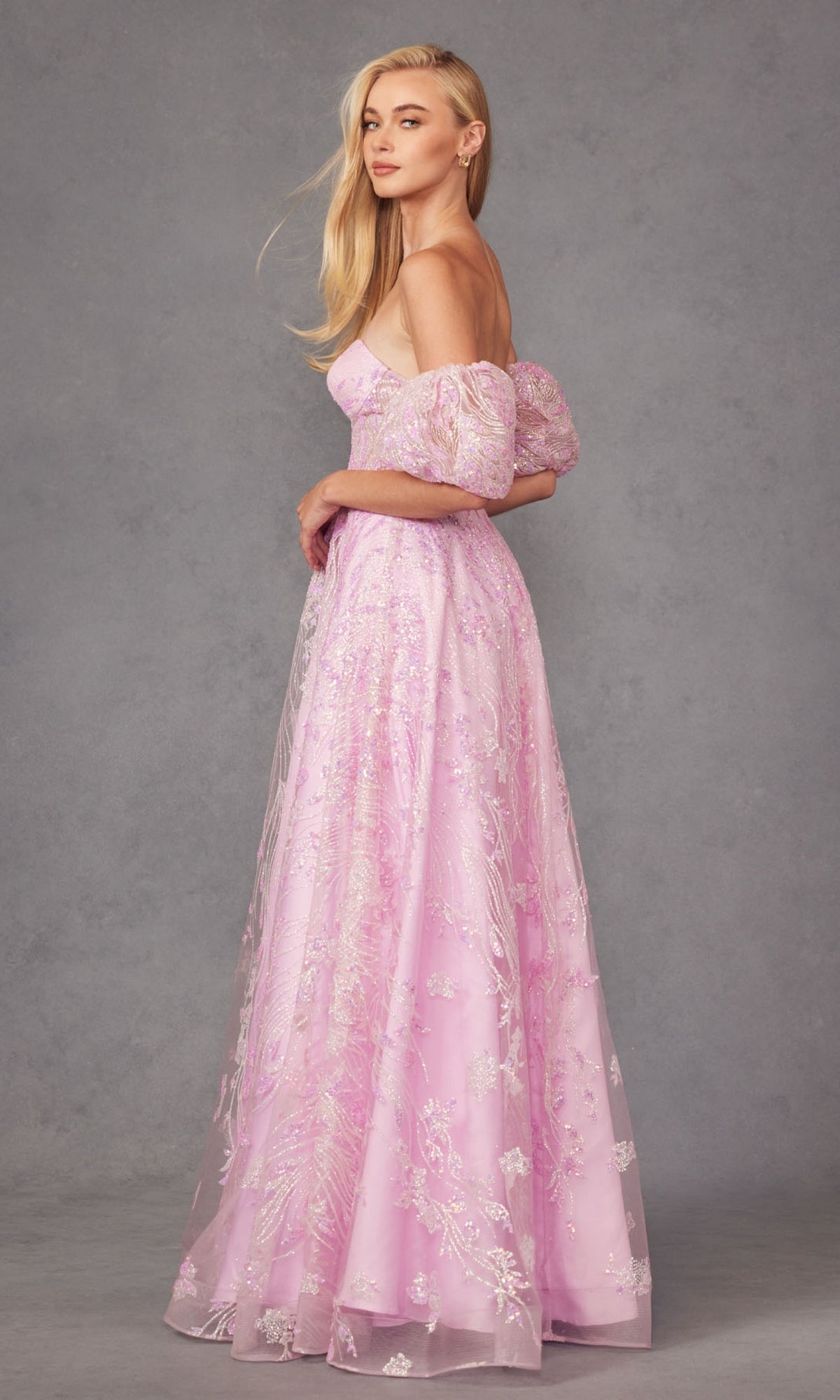 A woman stands in profile wearing the Puff-Sleeve Strapless Long Glitter Prom Dress 2404, a floor-length, off-the-shoulder gown with floral embroidery in light pink, set against a gray background.
